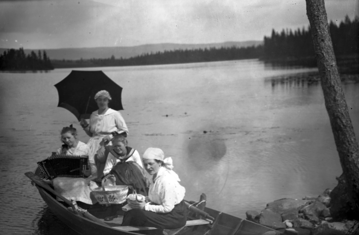 Fire kvinner i en båt ved Lisjøen.En kvinne med trekkspill og andre med paraply.