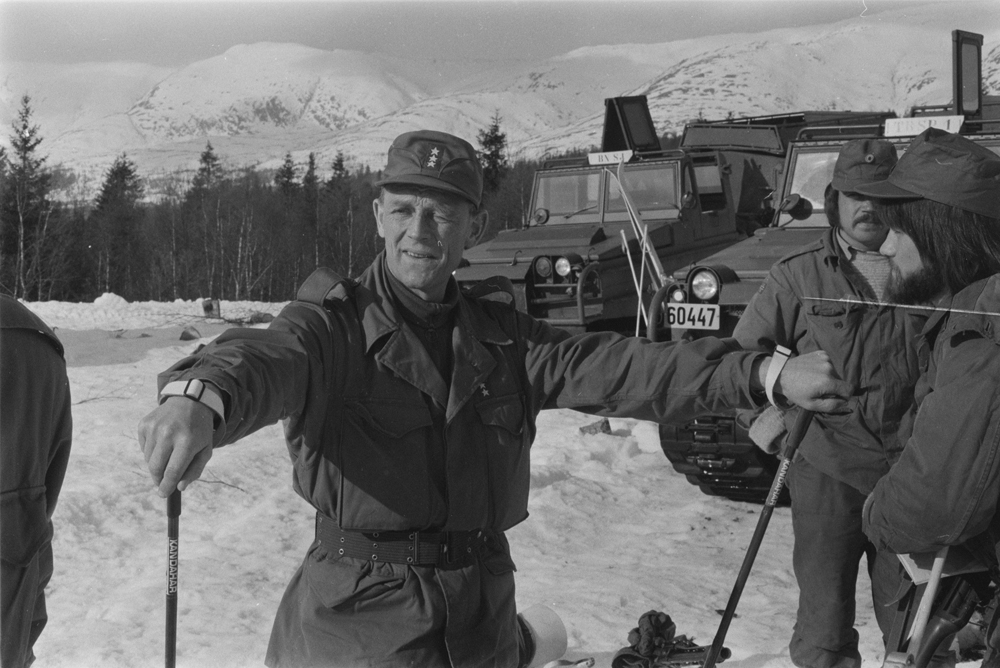 Repetisjonsøvelse på Drevjamoen. 
Kaptein Øyen med skistaver mellom soldater, bandvogner av typen Volvo BV202N i bakgrunnen. Den ene har registreringsnummer 60447