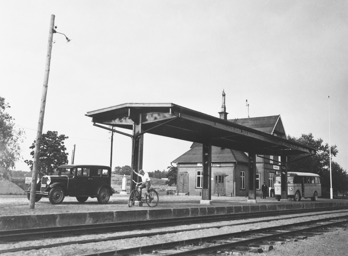 Åkersberga järnvägsstation, en Pojke på cykel, samt en buss och bil på plattformen.
