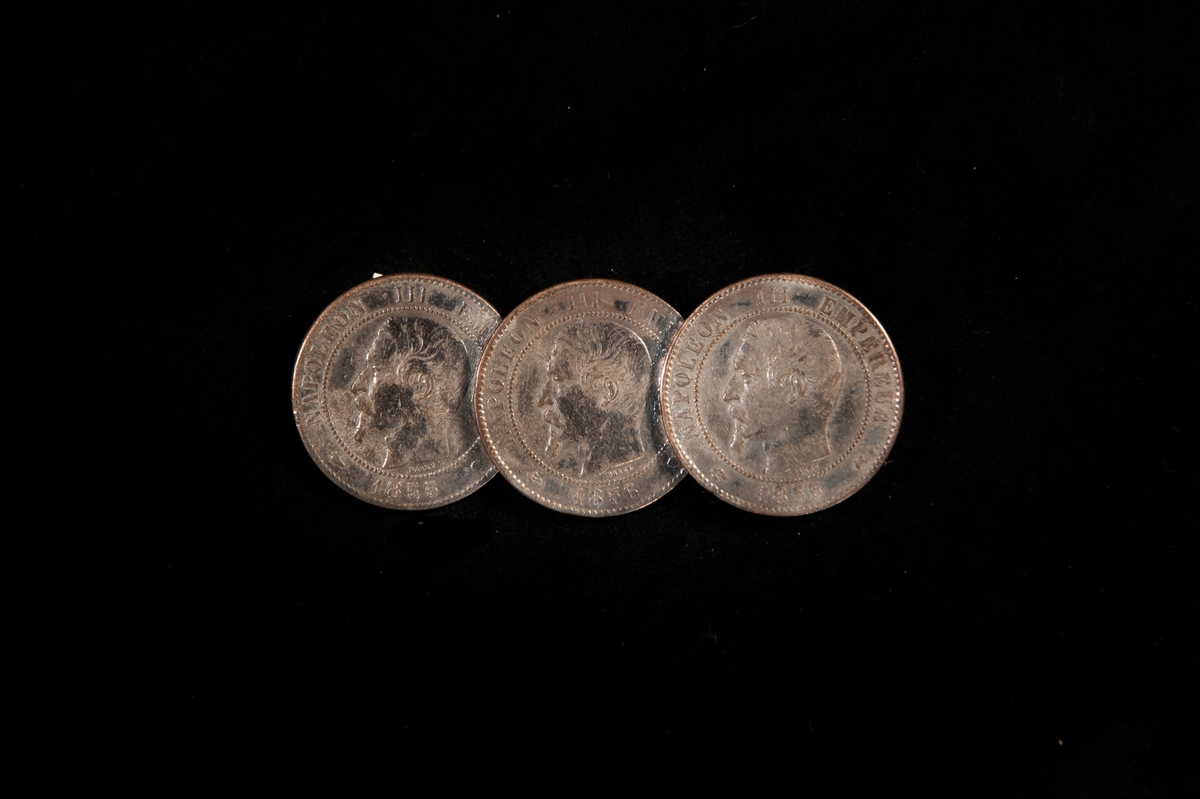 En rektangulär brosch, bestående av tre franska mynt (3 st. 10 centimes) från Napoleon III:s tid (reg. 1853-1870). Mynten, från 1855, 1856 och 1855 är lagda omlott.