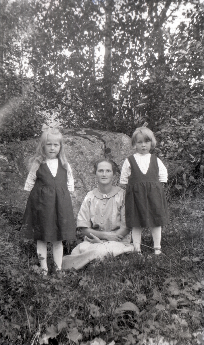Portrett av mor sittende utendørs med to døtre.