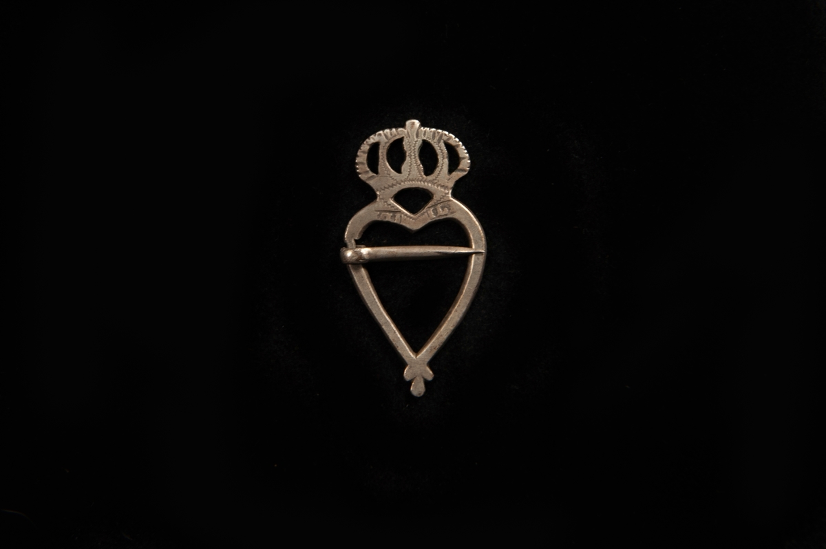 Ett hjärtformat spänne av silver med genombruten krona överst.