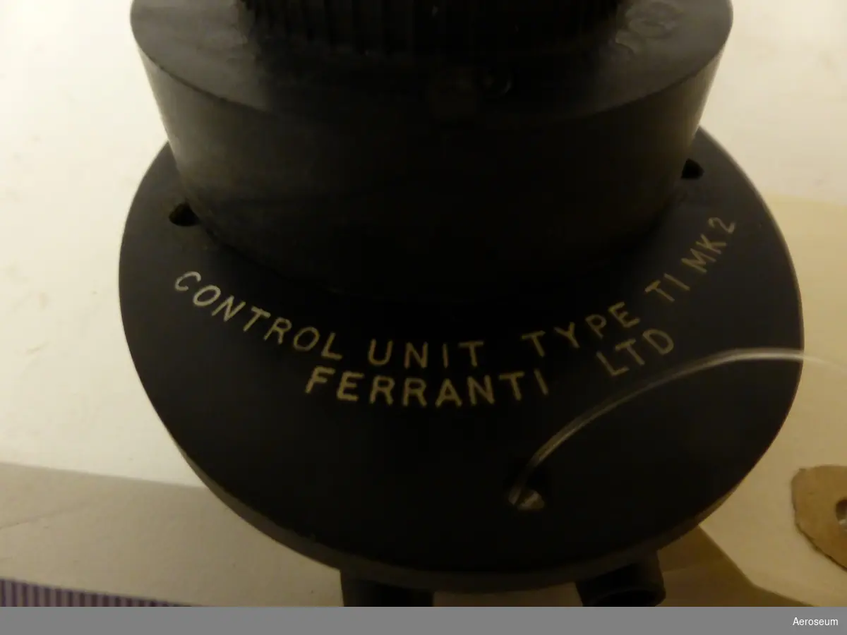 En kontrollenhet för luftbroms i Fpl 34 (J 34, Hawker Hunter). Den är gjord i svart metall. På föremålet går det att läsa: "CONTROL UNIT TYPE TIMK 2 FERRANTI LTD" på undersidan av föremålet går det också att läsa datumet "FEB 1960".
