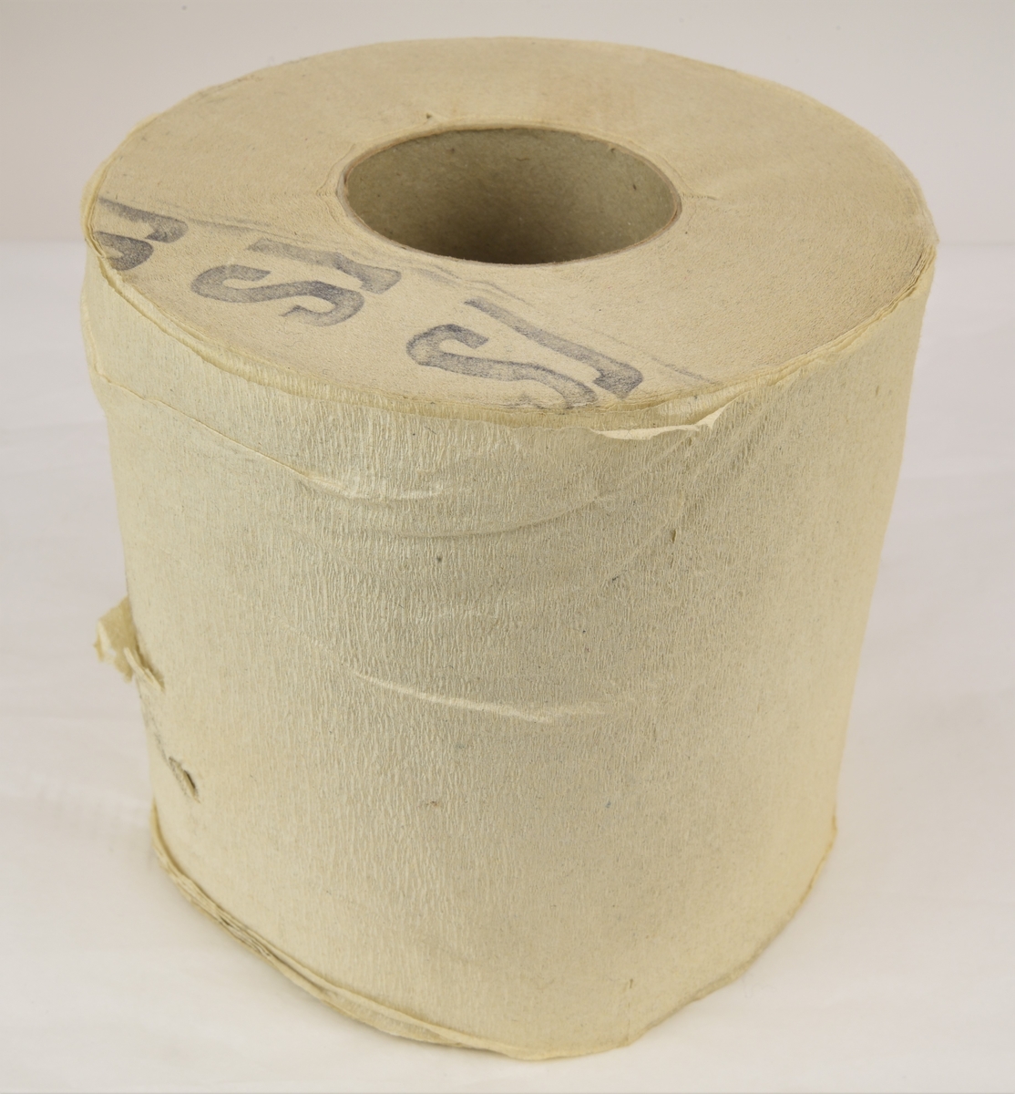 Toalettpappersrulle av svagt kräppat papper. Rullen är stämplad SJ på ena sidan med en mörk färg.