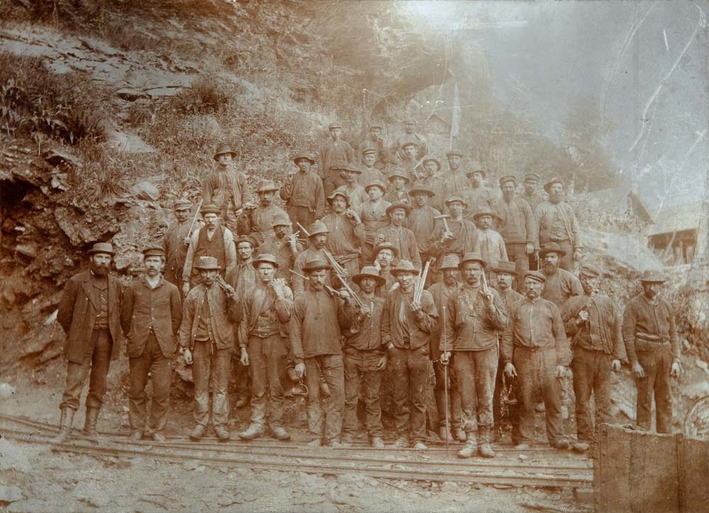 Gruppebilde av arbeidere i hatter og arbeidsklær. Kanskje gruvearbeid.