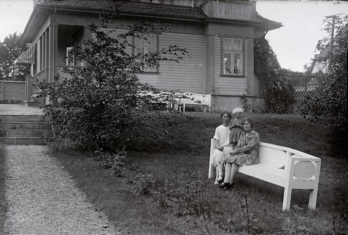 Kvinne med to døtre på benk foran hus. .Motivene i Opsangers glassnegativer ble brukt som postkort. .Nedre Torfæus gate i dag ..Glassnegativ fra Bokhandler K. Opsanger.