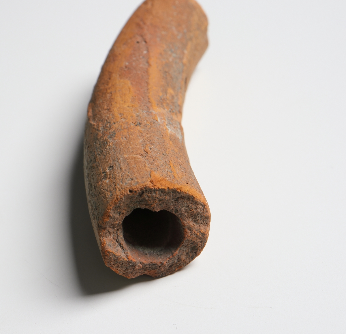 Del av ett ihålig snurrat horn (blåsinstrument). Cylindriskt rör med lätt böjd form av yngre rödgods. Tillverkad i regionen Schleswig - Holstein i Tyskland.