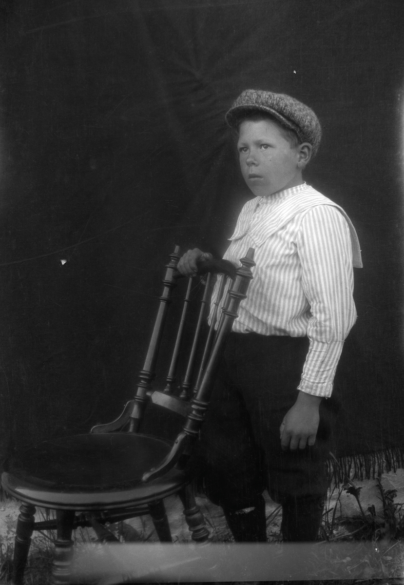 Portrett av en gutt stående med en stol.