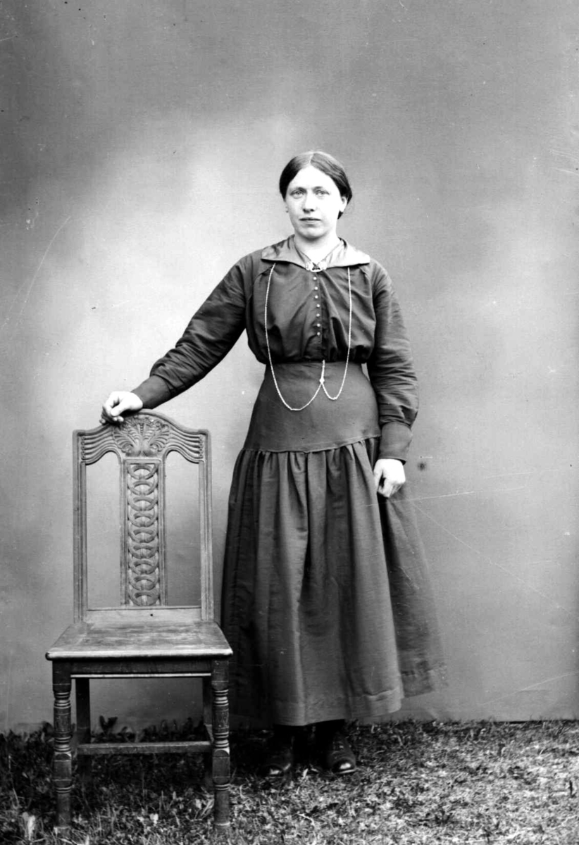 Portrett av kvinne ved siden av en utskåren stol.