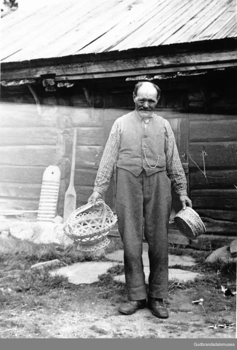 Amund Plasskveen (f. 1869) med sjølvlaga sendingskorg og ostetæje. Ved veggen står ei tullarfjøl og ei skjeltreko