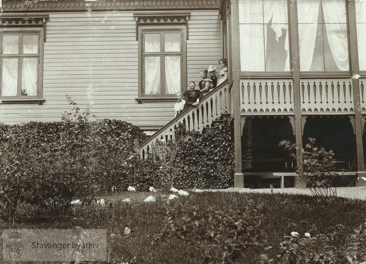 Kvinner av familien Monsen står i trappen opp til glassverandaen.