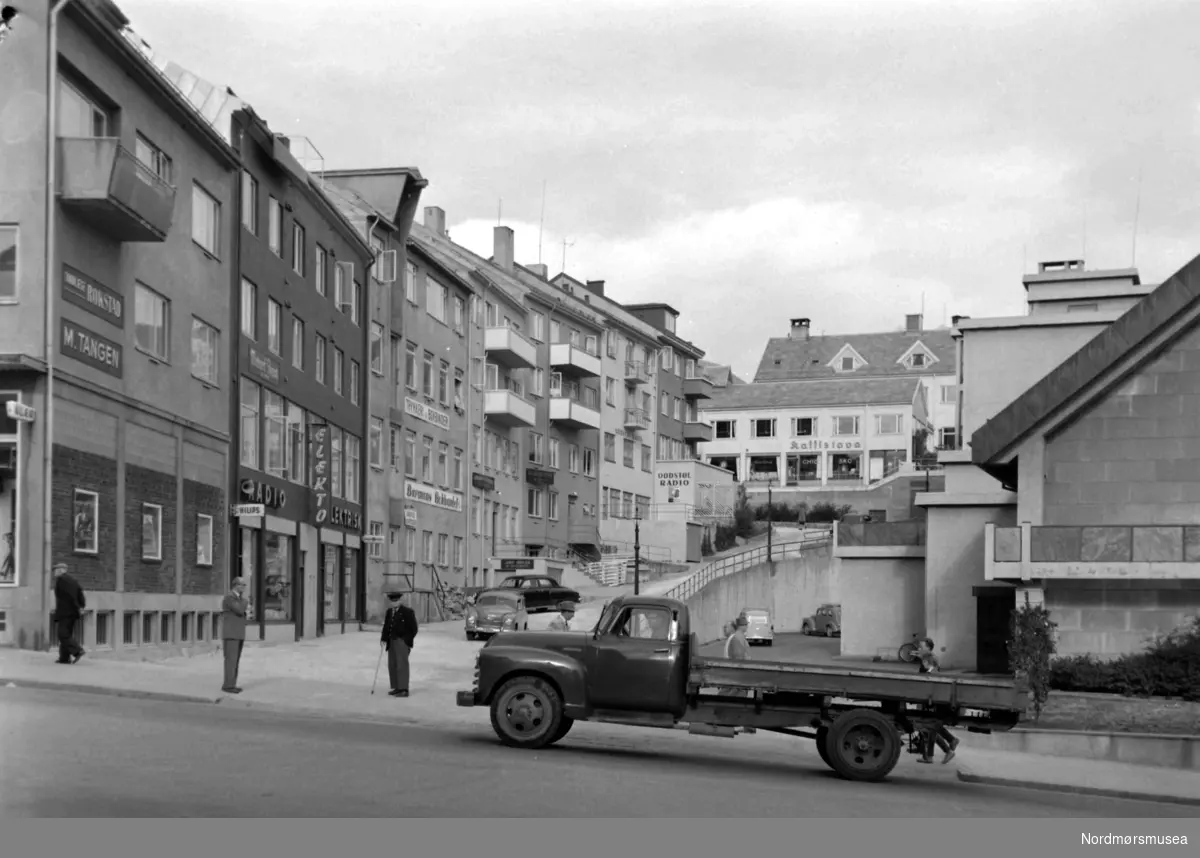 Foto av en lastebil i Kaibakken på Kirkelandet i Kristiansund, med bla.a. Rådhuset like bak. Fotograf er Nils Williams. Fra Nordmøre museums fotosamlinger.