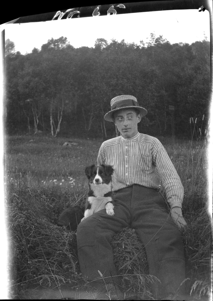 Ung mann med stråhatt og hund, fotografert sittende ute på marka.