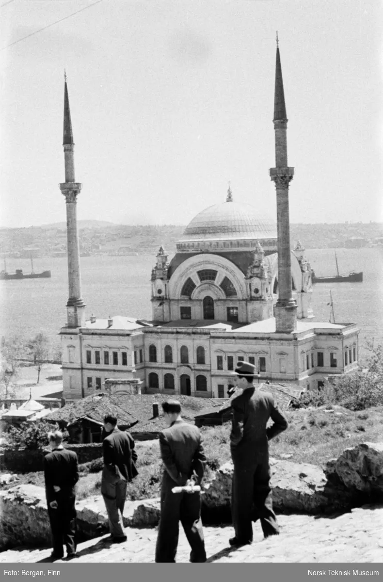 Gruppe på fire personer i landskap med en moske og med sjø i bakgrunnen