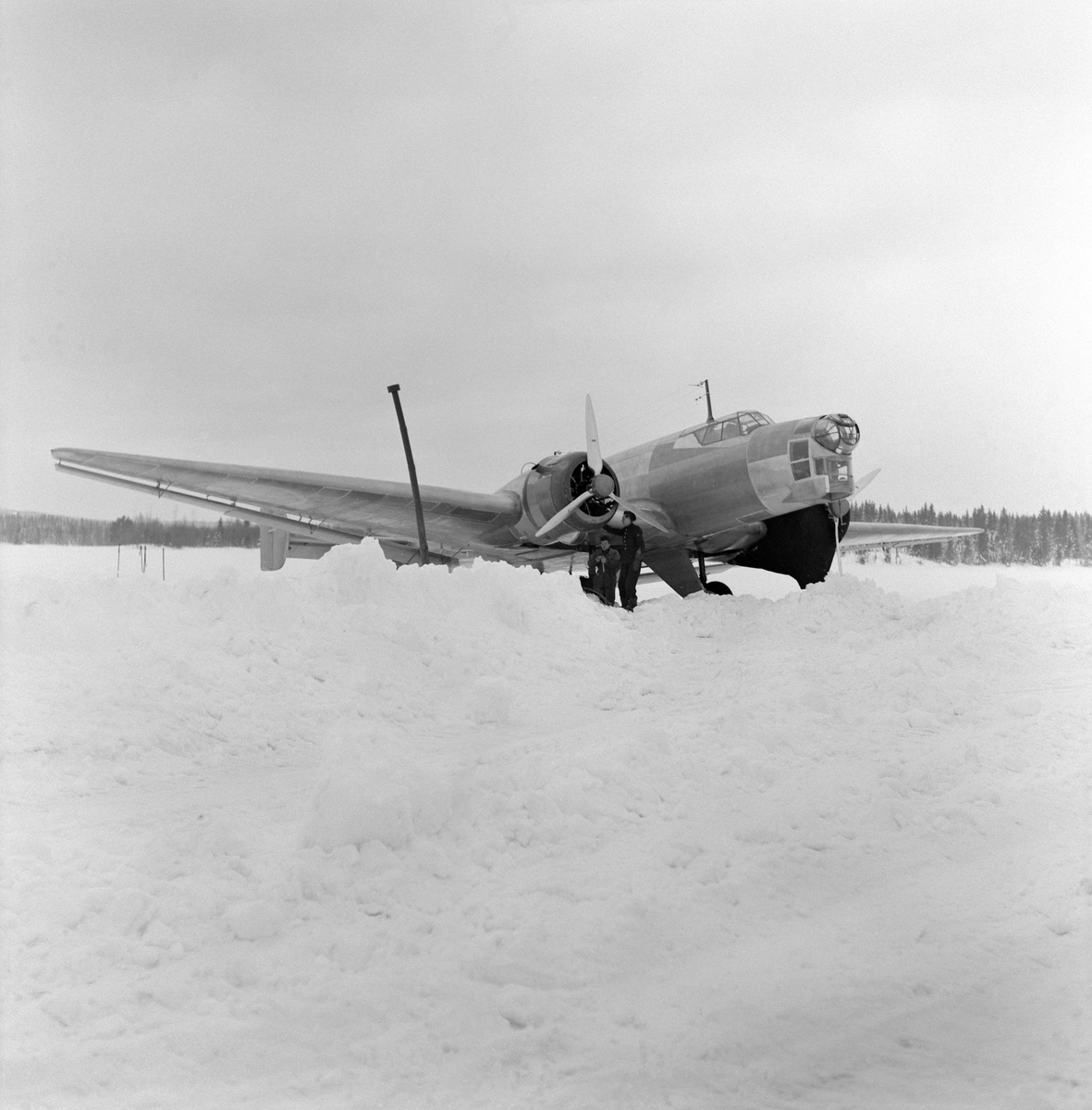 Flygplan B 3 nödlandad på Storsjöns is efter flygning i hårt väder i februari 1946. Flygvapenpersonal vid flygplanet. Vy snett framifrån.