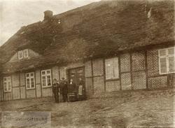 To menn og to damer foran et hus i bindingsverk