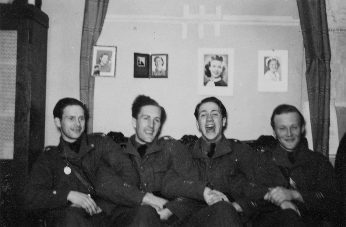 Samkväm på förläggning vid Svenska frivilligkåren i Finland, F 19. Gruppfoto av fyra militärer sittande i en soffa. På väggen bakom finns fyra porträtt av kvinnor uppsatta. Från vänster; Matti Sundsten, Thord Medalen, Roland Sahlberg, Thure Hansson.