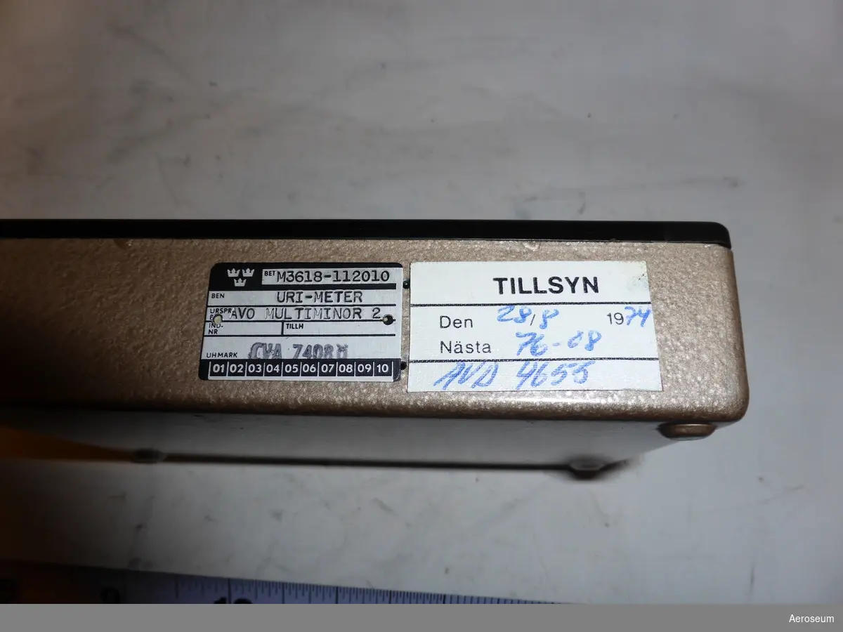 En svart URI-meter i brun läderförpackning. På lockets insida står det: "27922", detta nummer står även på själva URI-metern. På föremålets display står det "MULTIMINOR MADE IN ENGLAND".