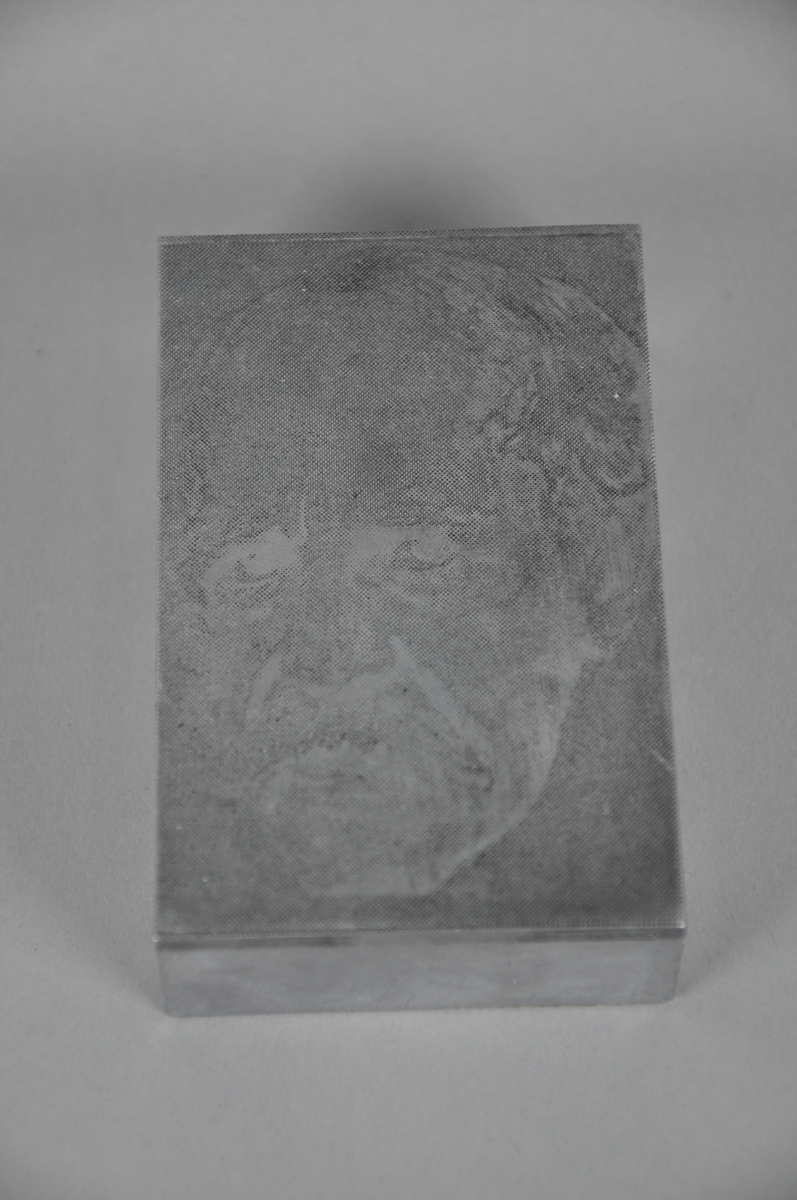 Trykkplate i metall med portrettmotiv.