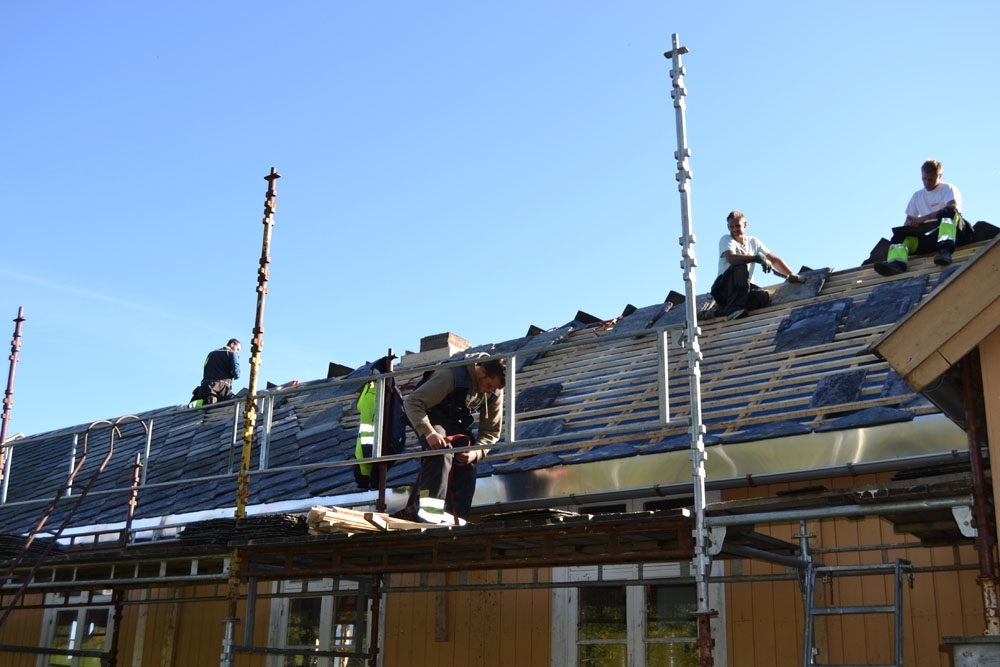 Leirfjord, Nedre-Leland. Entreprenørfirmaet, Einmo, legger om taket på Bergh-brygga (museet). Den nedbankede pipa blir murt opp igjen (midt i bildet). Snekkere fra Einmo tar en hvil på taket.