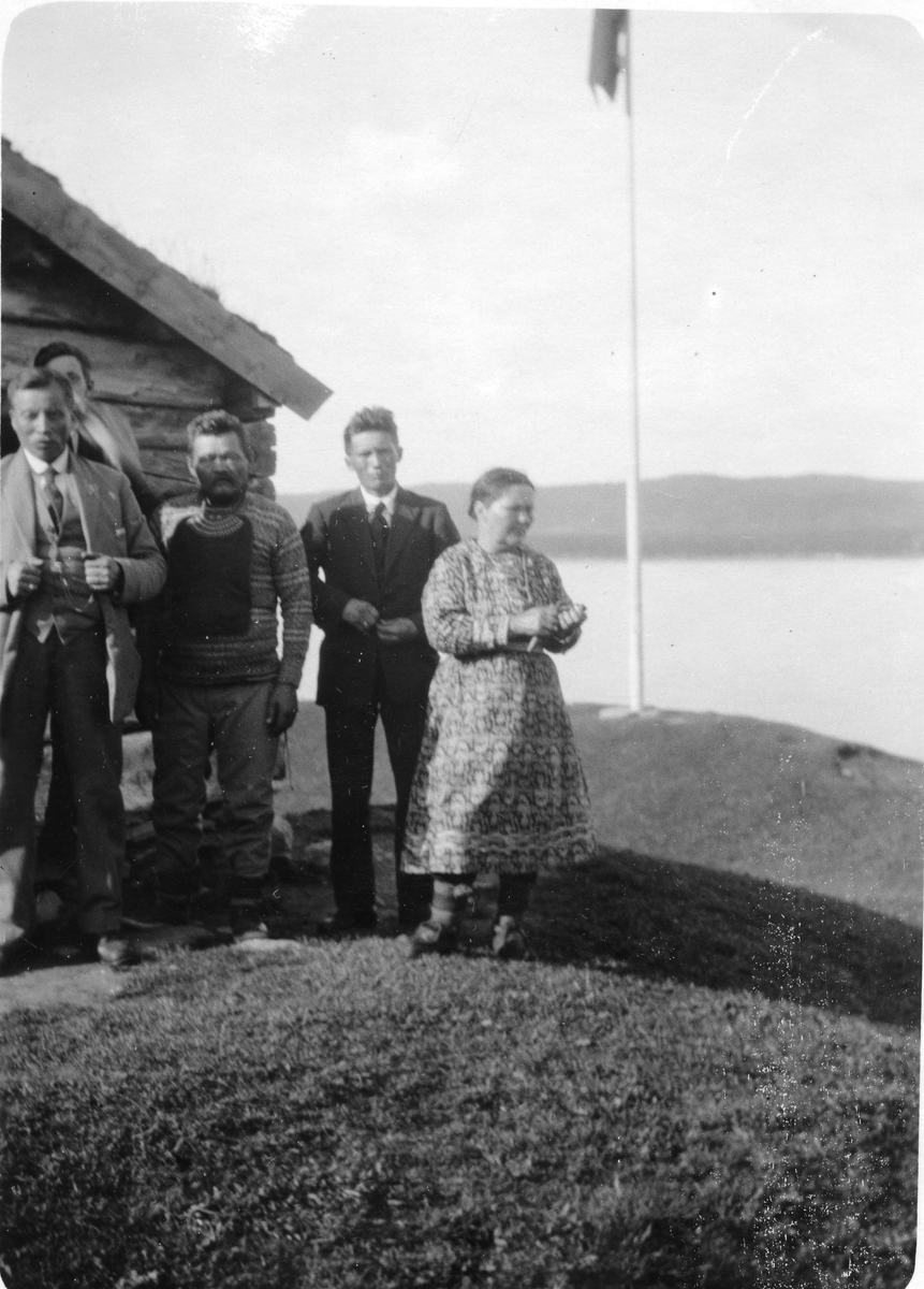Fem personer avbildet foran et lite hus ved et vann