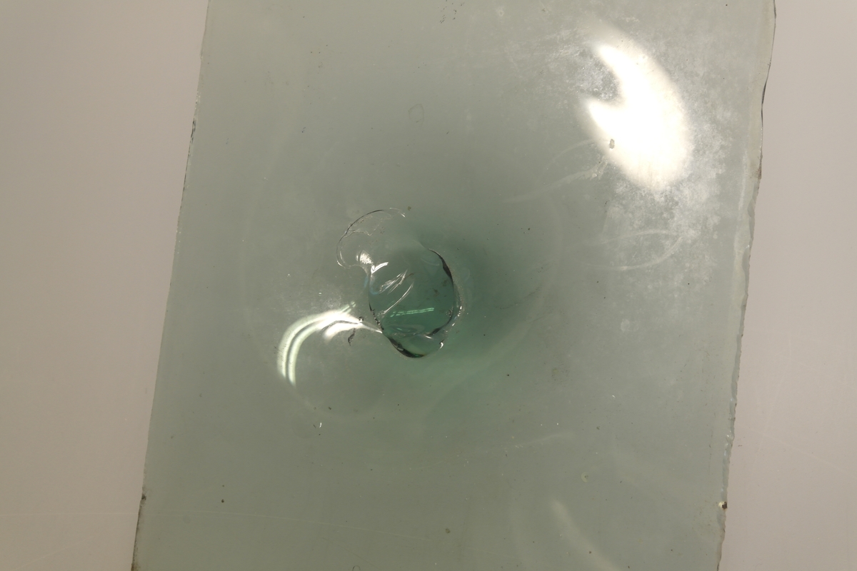 Grønnlig glassplate med "galle" i midten, dvs rester etter blåsepipen som ble brukt til dreiingen av glasset.