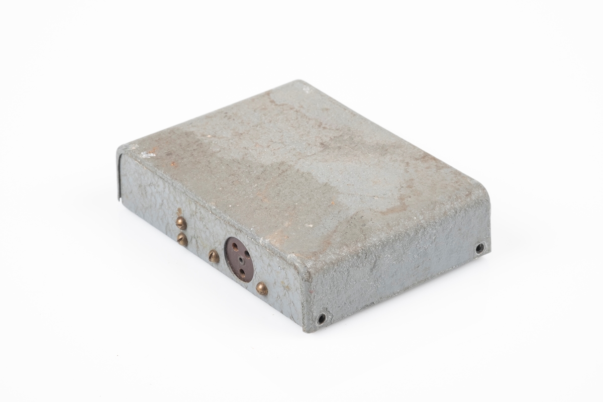 Tørrbatteri til kortbølgeradio med ytterplater er av metall som er lakkert i grått. På baksiden er det kontakt med 3 hull til kobling av ledning på radio.