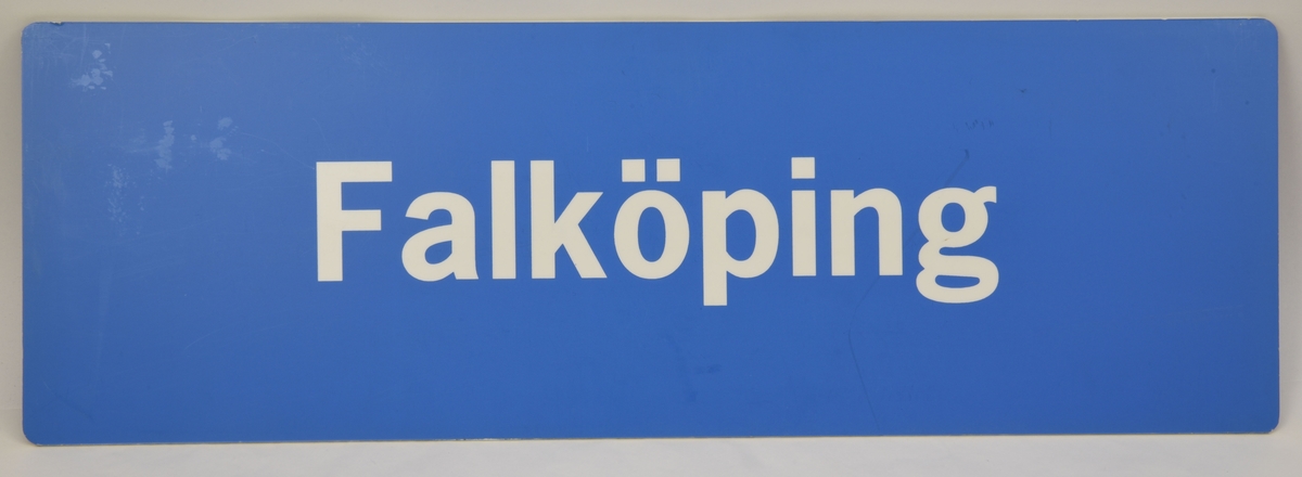 En blå avlång dubbelsidig destinationsskylt som har den vita texten "Falköping" på båda sidor.