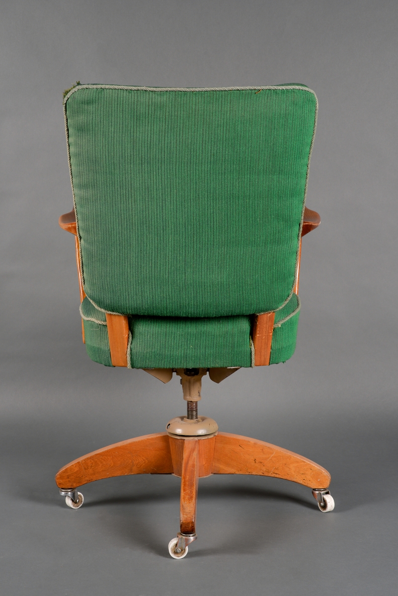 En dreibar kontorstol med armlener. Stolen er laget av heltre, huntonittplate og stålrørkonstruksjon. Den har sammenføyninger med skruer og lim samt treforbindelser. Det er grønt tekstil på sete og rygg. Langs kanten på setet er det grått pyntebånd (possement). Både sete og rygg er firkantet og har polstring bestående av farget ullblanding og skumplast. I setet er det metallfjærer. Stolen har fire bein med hjul på. Både treverket og metallet er lakkert.