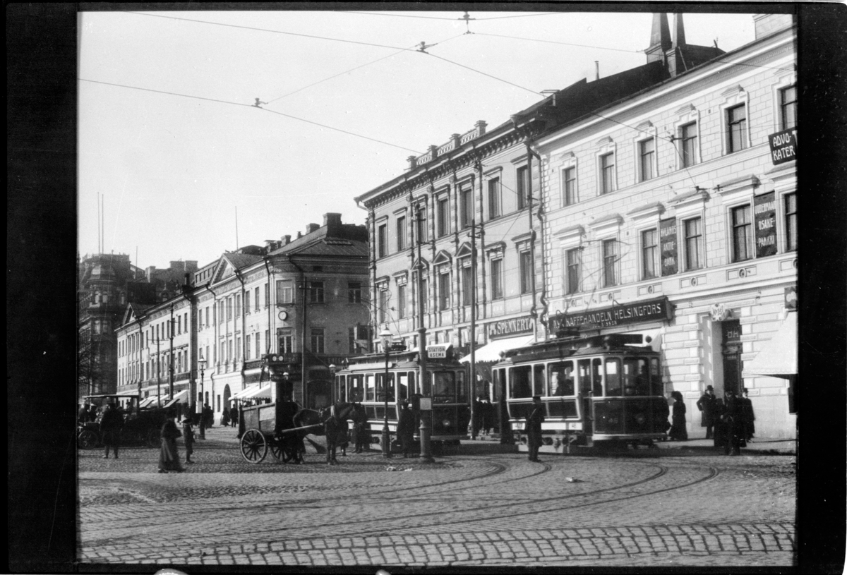 Vy över torget vid Södra kajen - Norra Esplanadgatan i Helsingfors. Helsingin Kaupungin Liikennelaitos, HKL spårvagn 46 och 37 ses mitt i bild, till vänster om vagnarna ses en hästtransport.