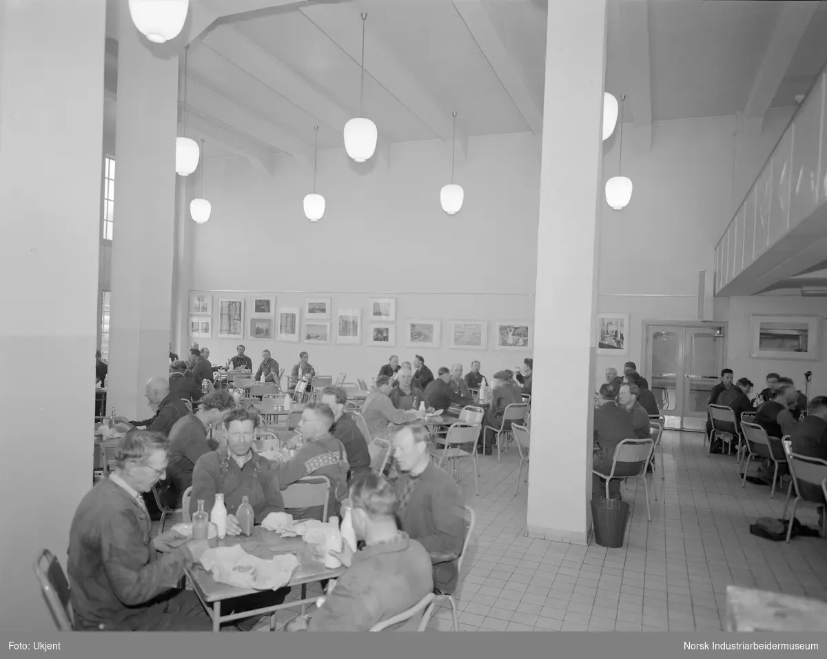 Interiør fra Velferden. Personer samlet innendørs. Arbeidende menn samlet til lunsj.