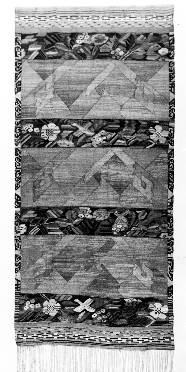 Foto (svart/vitt) av en rektangulär bonad i haute-lisse, med fågel- och blomstermotiv.

Inskrivet i huvudbok 1983.