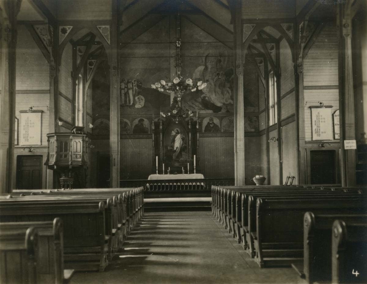 Interiør til Hammerfest kirke før ødeleggelsene under andre verdenskrig. Alter med altertavle, malerier, prekestol, døpefont og kirkebenker.