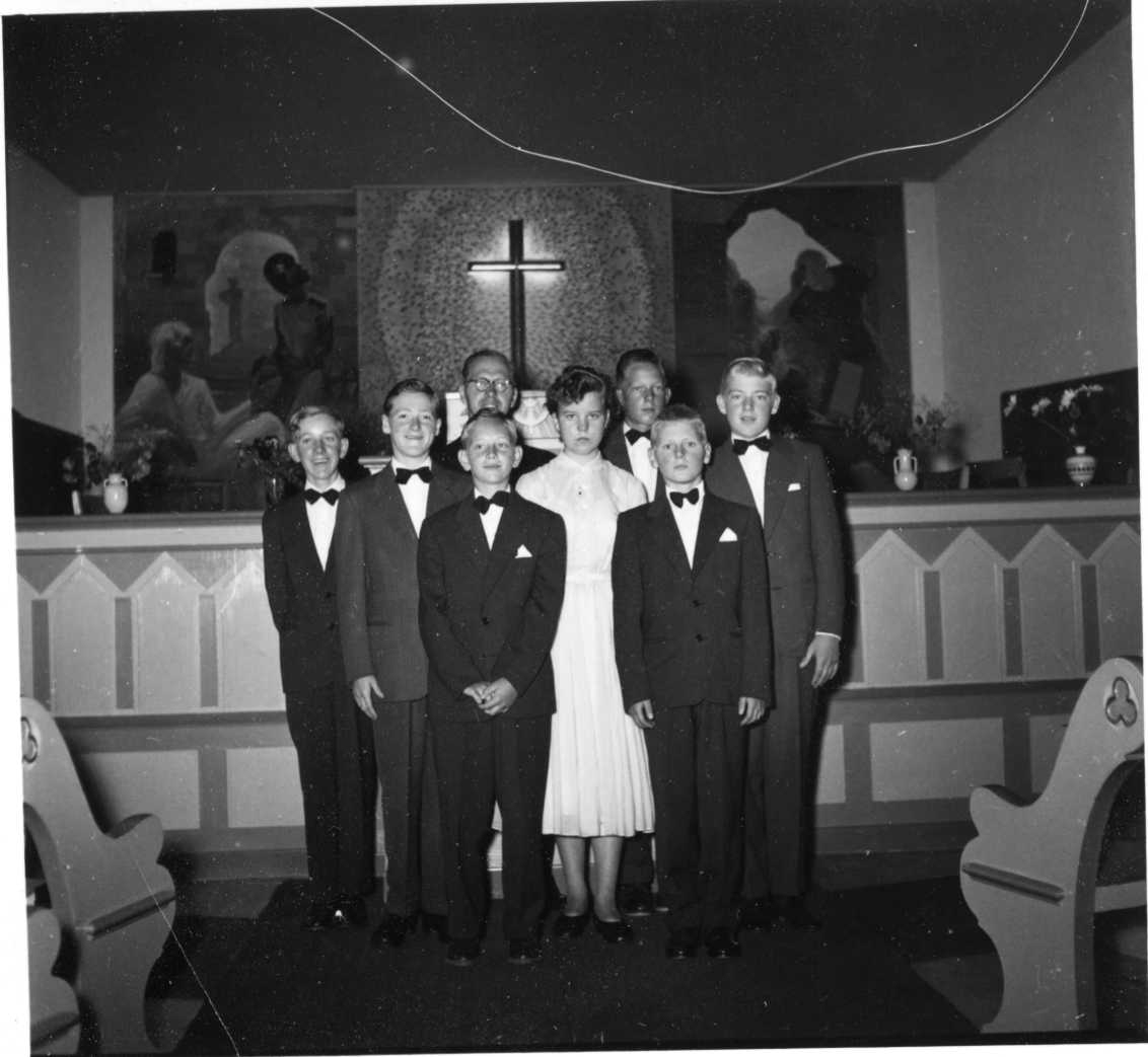 En grupp finklädda ungdomar uppställda i Missionskyrkan i Gränna, troligen konfirmationsgrupp. Pastor Josef Olsson står i bakgrunden. Till vänster står Lars Jonsson och längst fram till höger står Lars Rosenkvist.