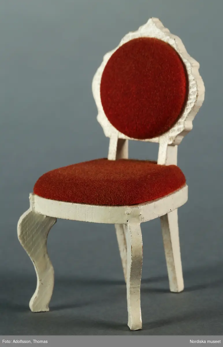 Möblemang med a) soffa och b-c) två stolar i bondrokoko tillverkad av vitmålat trä och rött sammetsliknande tyg. Fabrikstillverkad. Hör till inredningen i hallen på första våningen i dockskåp NM.0331721+. och är placerad längs långväggen, mittemot hallspegeln.