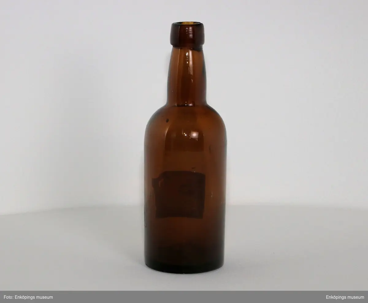 Brun flaska med etikett " Klass..., pilsnerd..., Aktiebola..., Enköpings Ångbr.... Märkt ibotten med " ÅRNAC"?.
