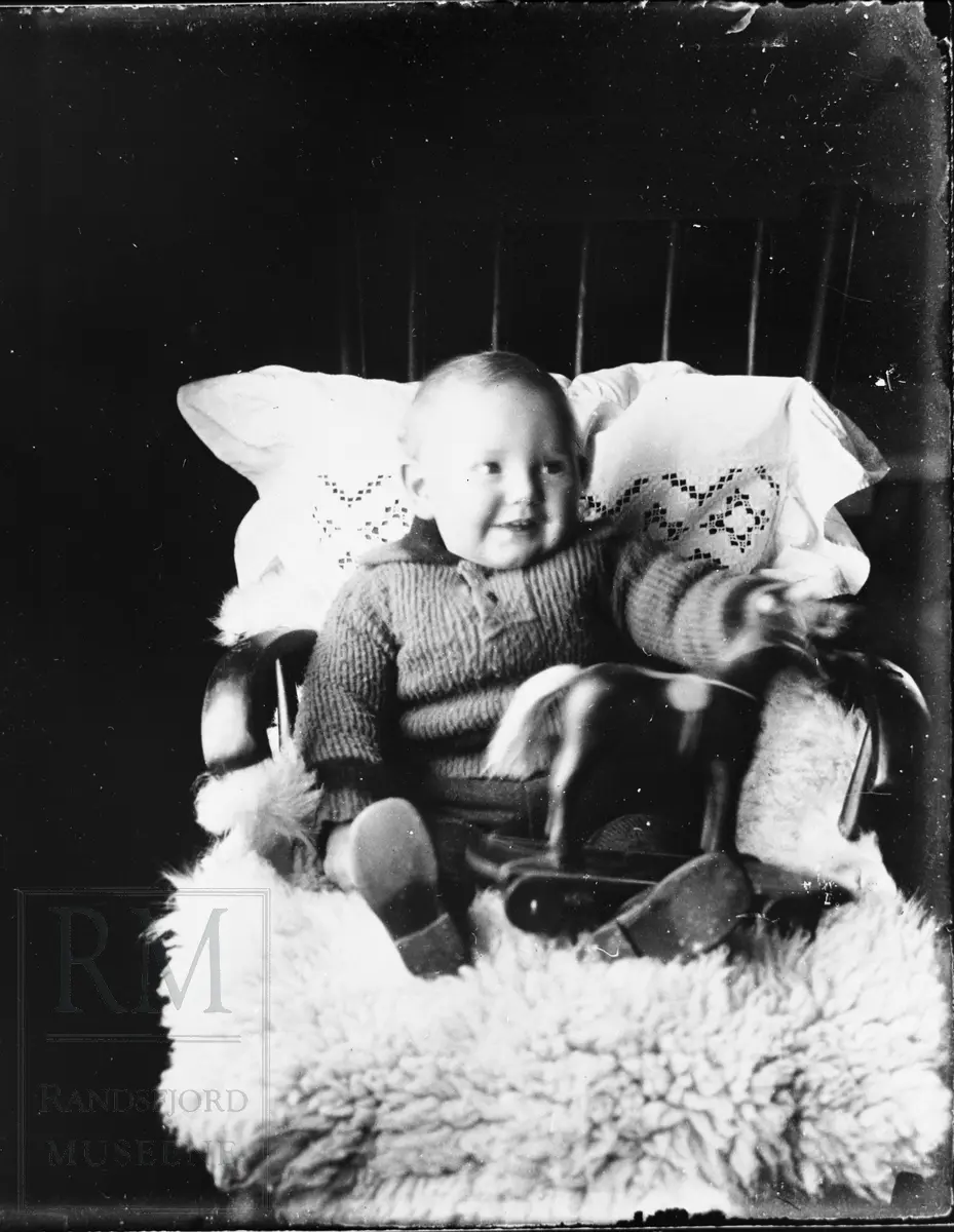 Et liten gutt sitter i en stol med en liten lekehest i fanget.