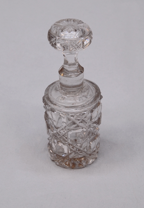 Gräddvit flaska (A) av elfenben, med kork (B) och botten(C) som går att skruva loss. Inuti finns ytterligare en flaska (D) av kristallglas, med propp (E). 

Den yttre flaskan är formad som en cylinder som smalnar av upp mot korken. Botten på flaskan är klädd i filt. 
Den inre glasflaskan är formad som den yttre, och har kvadratiskt rutmönster i relief. Proppen är halvklotformad och har samma dekorationer som flaskan på sidorna, samt ett blommönster i relief ovanpå.