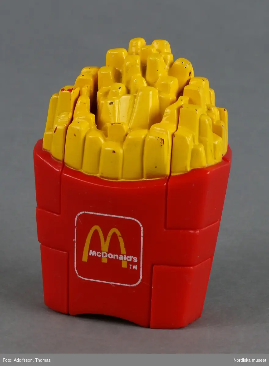 Leksak i form av pommes frites, en vanligt förekommande maträtt på snabbmatställen. Vissa delar är rörliga och kan fällas ut, varvid en gul djurfigur med huvud och svans framträder. Tillverkad av plast med tre skruvar av metall. På framsidan tryck med McDonald's logotyp.