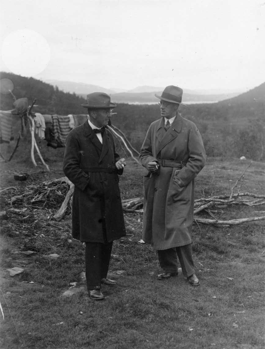 Två män i hatt och rock med cigarett i händerna står och samtalar i ett fjällandskap. Mannen till höger är Sven Jerring. Bakom dem står det en träställning där det hänger textilier och renskinn.
