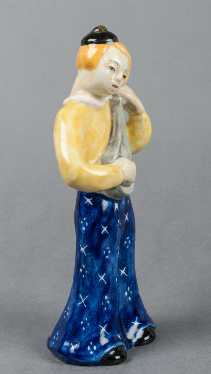 Figurin Zahra, kvinna spelande mandolin, glaserad i främst gult och blått. Tillverkad av Gefle Porslinsfabrik, formgiven av Märta Willborg 1937.