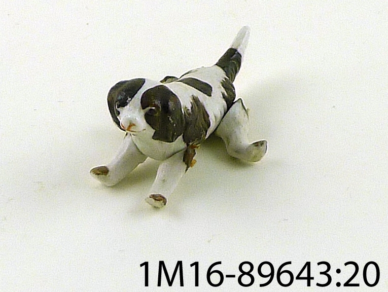 Figurin, hund av porslin, brun och vit, ligger ner eller står upp beroende på hur en placerar benen.