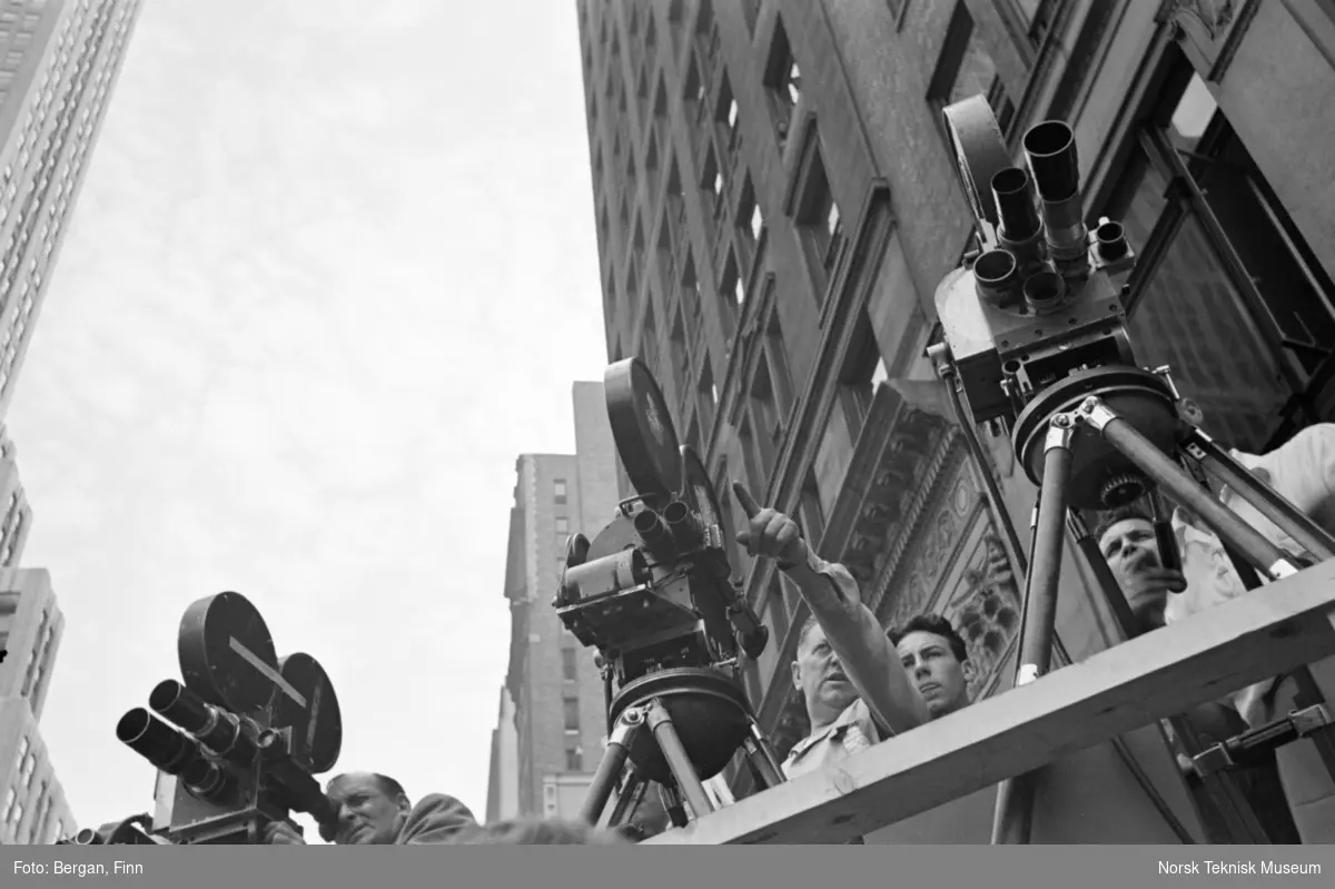 Fotografer med filmkameraer sett nedenfra med høyhus i bakgrunnen