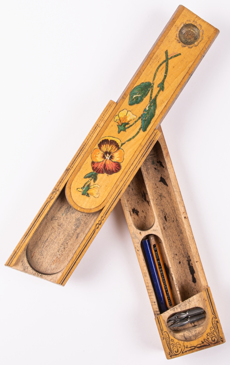 Pennskrin av trä med skjutlock. På locket en målad pensé. På undersidan står: 1908 elna Östlin. I skrinet ligger tre pennstift av metall.