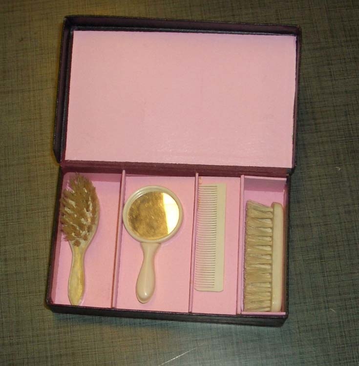 Etui med kam, hårbøste, speil, klesbørste. Etuiet er fôret med rosa stoff.