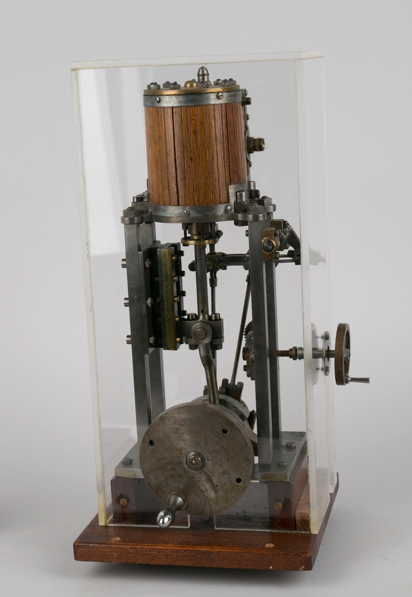 Dampmaskinmodel, en-sylindret i tre og metall med dreiehjul montert på to side. Montert i plexiglassklokke.