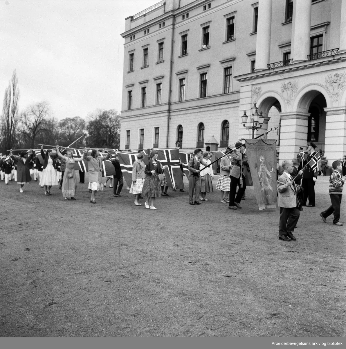 Barnetoget passerer slottet. Flaggborg. Fanen til Gamlebyen Skole. 17. mai 1957.