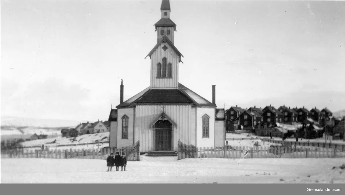 Tre barn står foran Kirkenes kirke, Haganes i bakgrunnen, mars 1922.