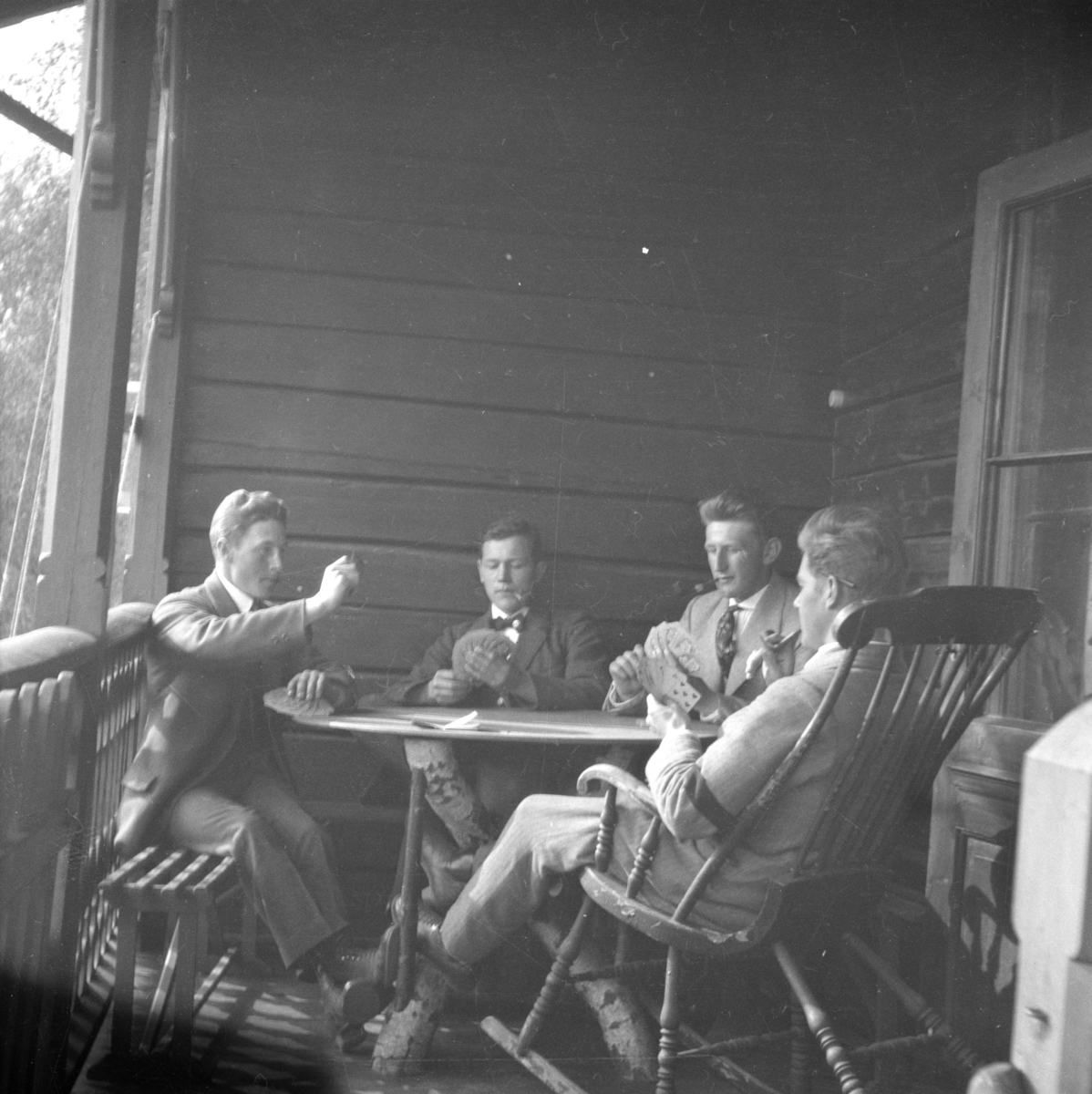 Fire menn på veranda som spiller kort.