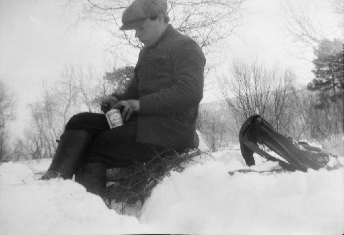 Mann i skyggelue og ryggsekk, med en hermetikkboks. Rast i snøen.